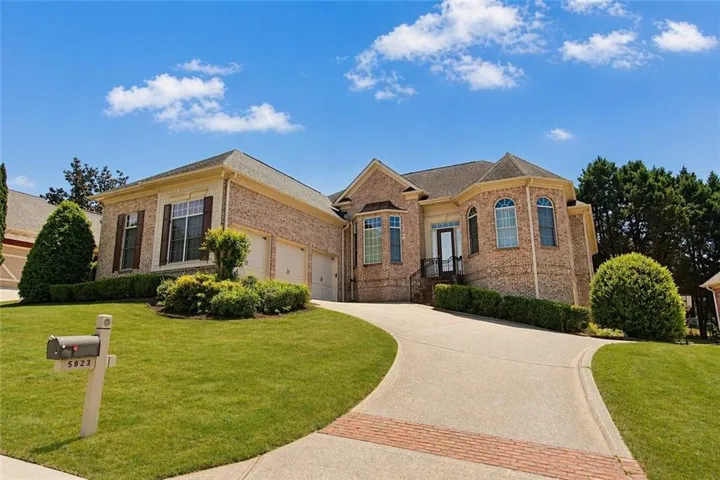 Brick exterior residence featuring a curved paved driveway with brick accents, an integrated two-car garage, and established landscaping