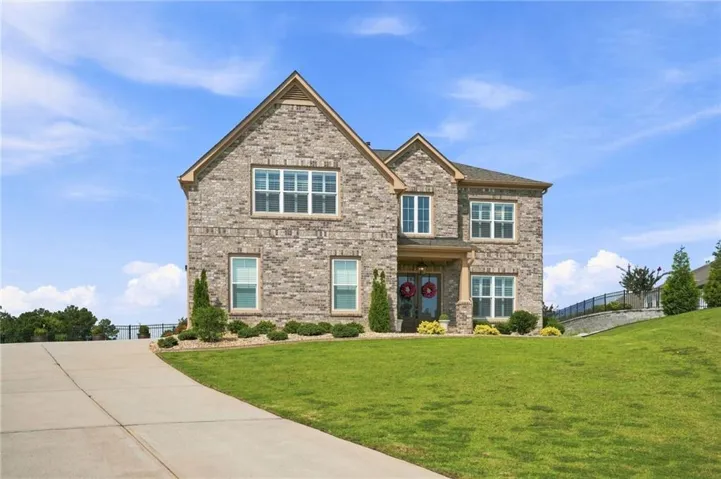 Stone exterior with multi-pane windows and gabled roofline, positioned on an expansive sloped lawn with mature landscaping and a concrete driveway approach