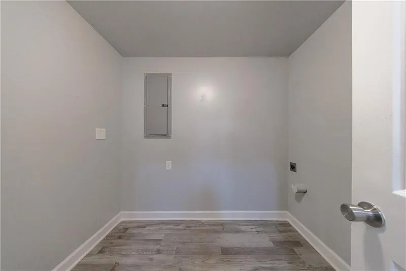 Laundry area with hookup for an electric dryer, electric panel, laundry area, light wood-style flooring, and baseboards