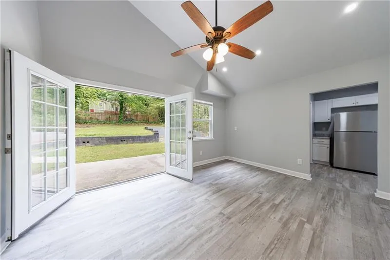living room with baseboards, light wood-type flooring, a ceiling fan, and high vaulted ceiling