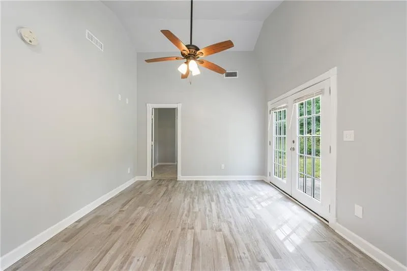 Spare room featuring light wood finished floors, visible vents, and high vaulted ceiling