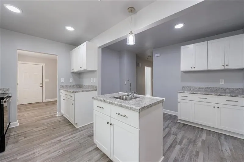 Kitchen with light wood-type flooring, light countertops, white cabinets, and a sink