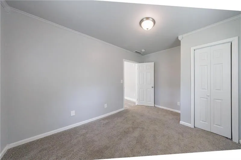 Unfurnished bedroom featuring crown molding, visible vents, a closet, baseboards, and carpet floors