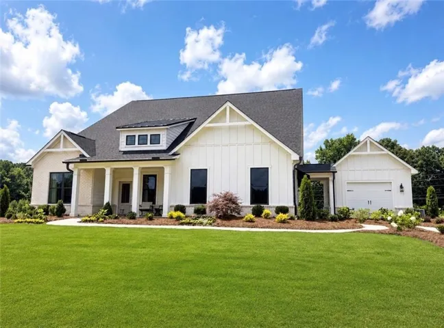 Contemporary farmhouse exterior featuring white board and batten siding, light brick accents, a dark shingle roof, a covered front porch with white columns, and a two-car garage with a white overhead door