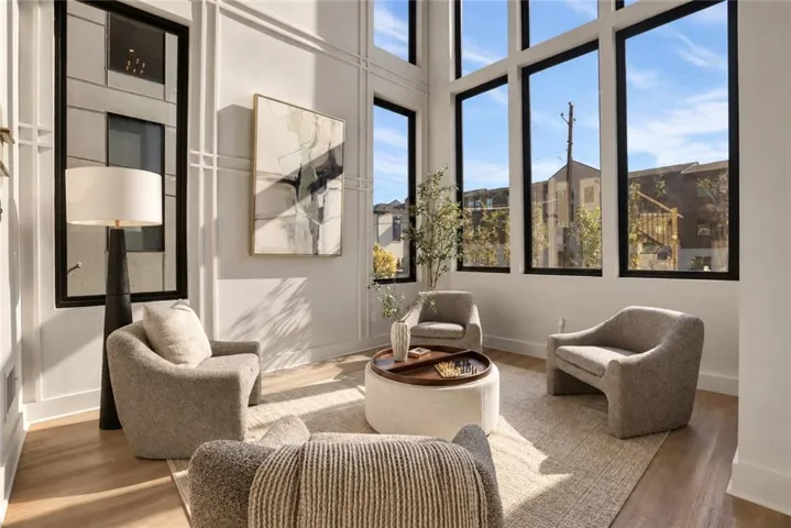 Double-height living space featuring expansive windows with black frames, decorative wall molding, and wood-finish flooring