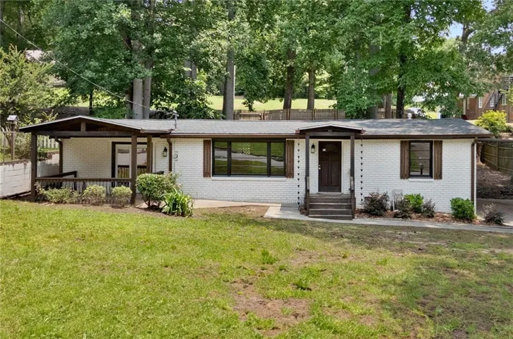 White brick exterior with dark trim and shutters, wood porch, and mature trees