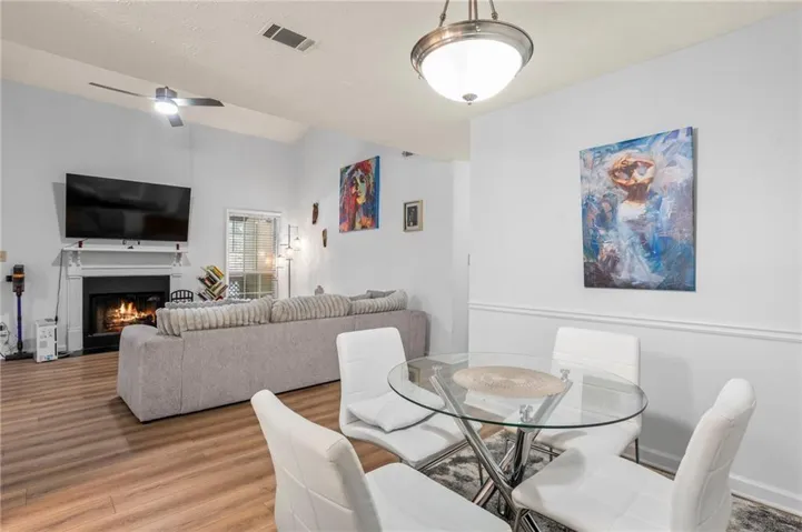 Vaulted ceiling with a ceiling fan, fireplace with a mantel, wood-finish flooring, and a dining area with a contemporary chandelier
