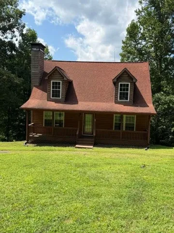 Cabin-style exterior with wood siding, a red shingle roof, and two dormer windows