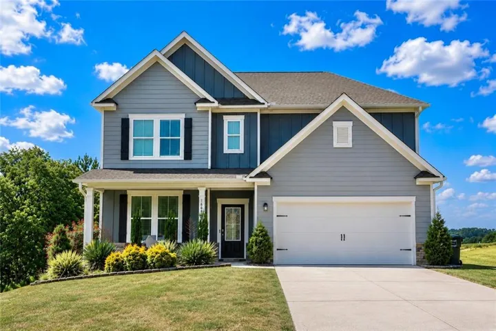 Two-story residence featuring light gray and dark blue siding, a two-car garage, covered entry porch with white columns, and a landscaped front yard