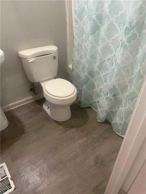 Bathroom featuring shower / bath combo with shower curtain, wood-type flooring, and toilet