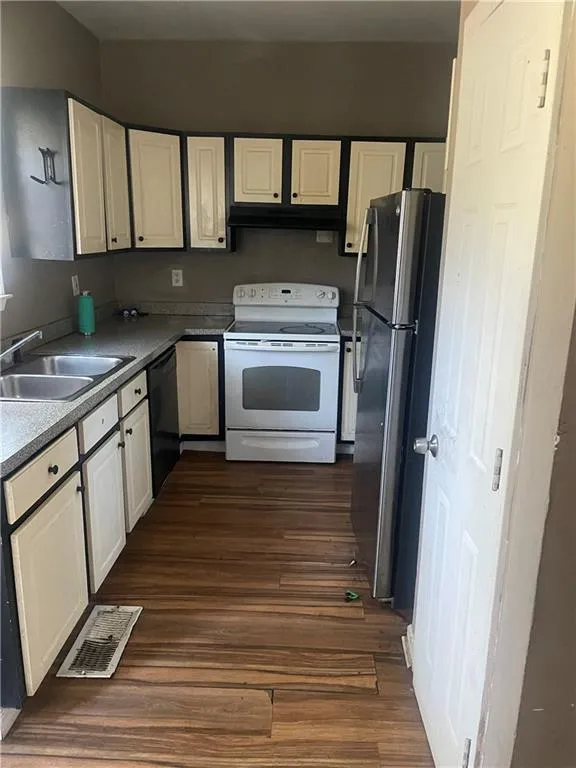 Kitchen with stainless steel fridge, white range with electric stovetop, sink, black dishwasher, and dark hardwood / wood-style floors