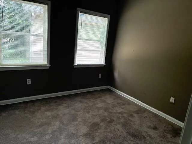 Spare room featuring dark carpet and baseboards