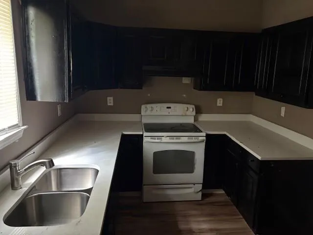 Kitchen with white electric range oven, dark cabinetry, light countertops, wood finished floors, and ventilation hood