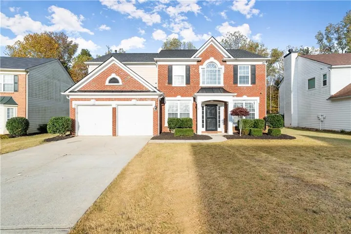 Brick facade with white trim, two-car garage, covered entry, front landscaping, and a paved driveway