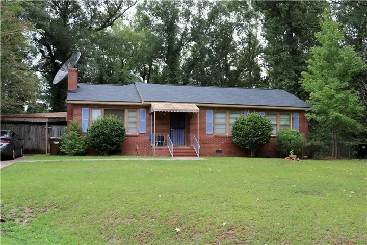 Charming brick ranch home featuring a welcoming front facade with blue-trimmed windows, covered entry portico, and a professionally landscaped front lawn anchored by mature shade trees and established shrubs