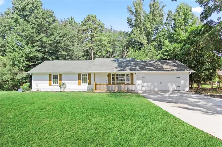 White siding exterior with wood shutters, front porch with wooden railing, attached two-car garage, and a concrete driveway