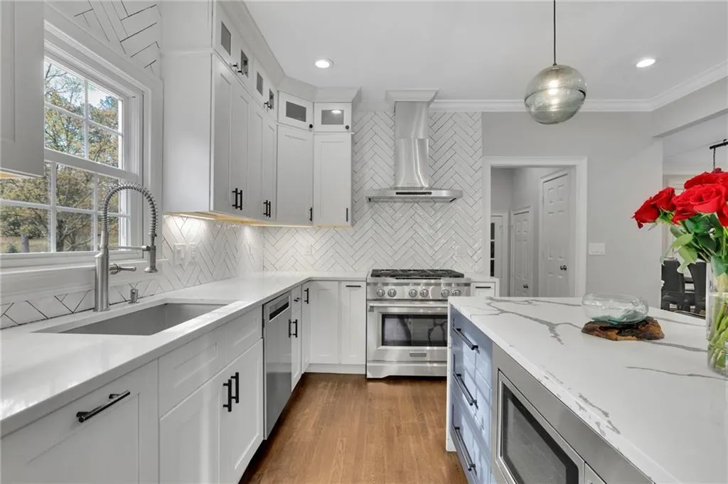 Kitchen with light stone countertops, stainless steel appliances, hanging light fixtures, dark wood-type flooring, and ornamental molding