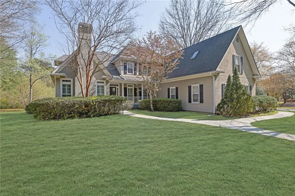 View of front of home featuring covered porch, a front lawn, stucco siding, a chimney, and roof with shingles
