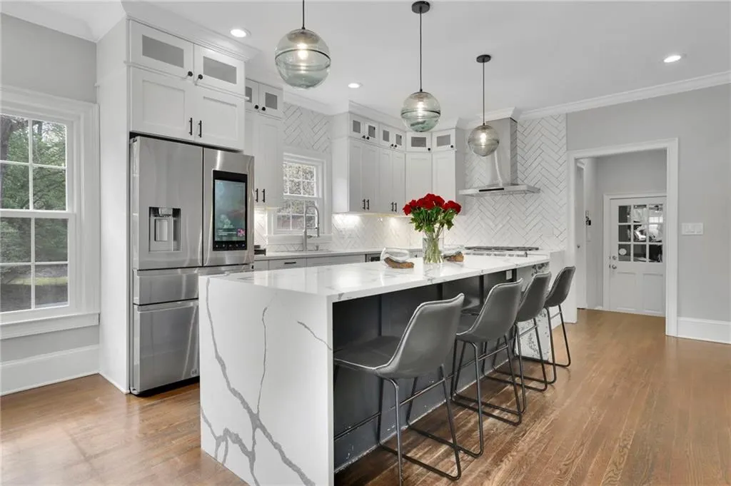 Kitchen with stainless steel appliances, light stone counters, glass fronted cabinets, a breakfast bar, and decorative light fixtures