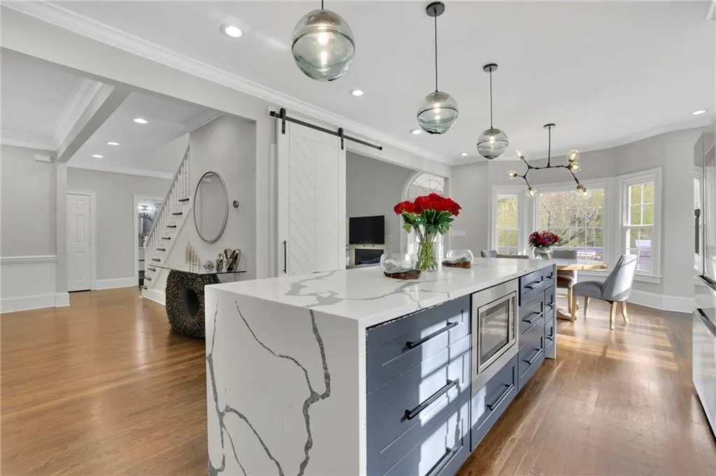 Kitchen with a barn door, a center island, light stone counters, decorative light fixtures, and ornamental molding