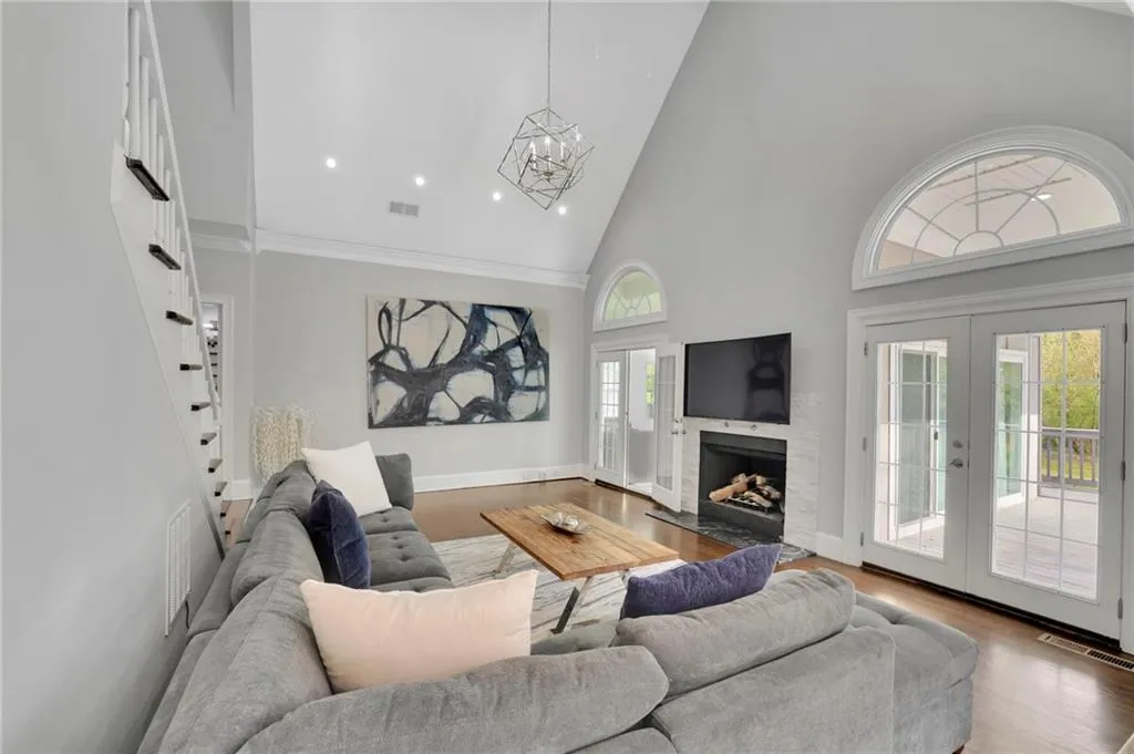 Living room featuring vaulted ceiling, wood finished floors, a high end fireplace, a chandelier, and french doors