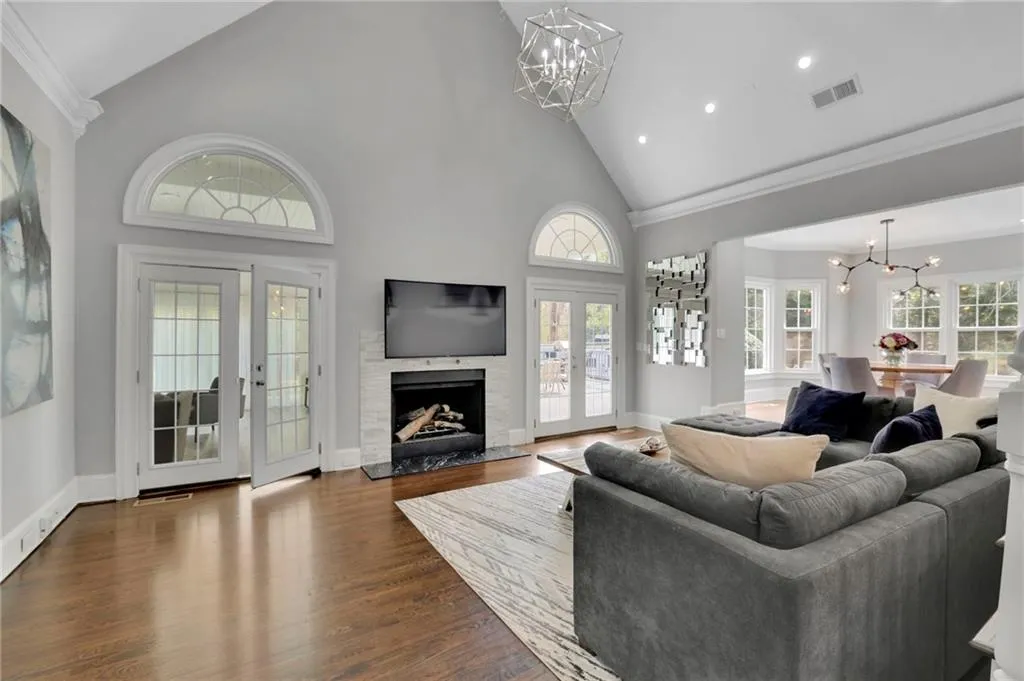 Living room featuring hanging lights, vaulted ceiling, a fireplace, dark wood-style floors, and crown molding
