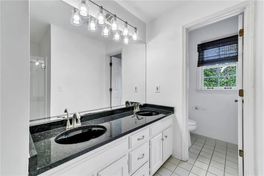 Shared bathroom featuring dual sinks, tile floors, toilet, and oversized vanity Shared bathroom featuring dual sinks, tile floors, toilet, and oversized vanity