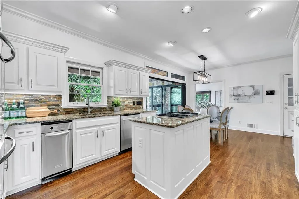 Kitchen featuring stainless steel appliances, wood-type flooring, white cabinets, pendant lighting, and a center island Kitchen featuring stainless steel appliances, wood-type flooring, white cabinets, pendant lighting, and a center island