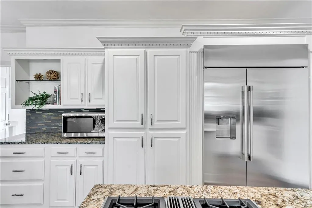 Kitchen featuring white cabinetry, backsplash, ornamental molding, stainless steel appliances, and dark stone countertops Kitchen featuring white cabinetry, backsplash, ornamental molding, stainless steel appliances, and dark stone countertops