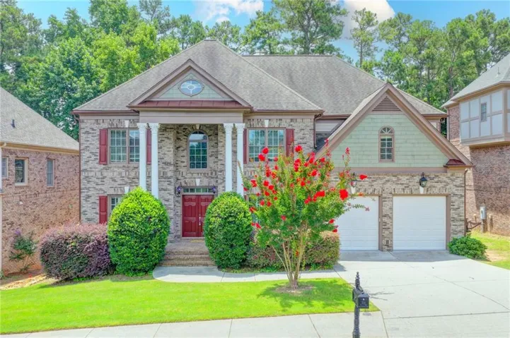 Brick facade residence featuring a covered entry with white columns and red double doors