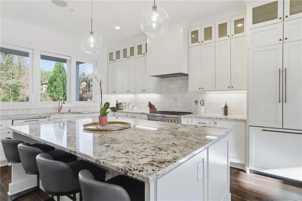 Spacious kitchen featuring a large island with seating, white shaker cabinetry, stainless steel appliances, and a tile backsplash