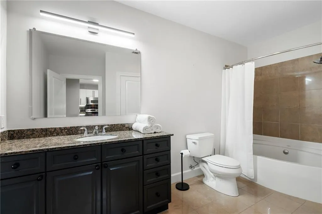 Bathroom featuring toilet, vanity, shower / bath combination with curtain, tile patterned floors, and baseboards
