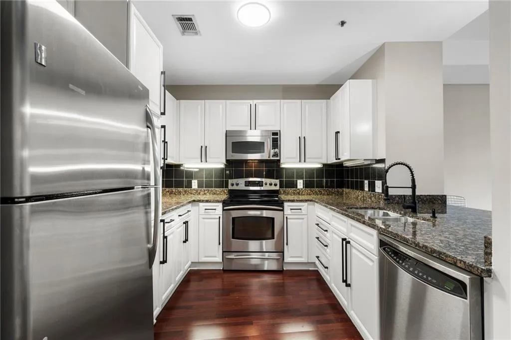 Kitchen with appliances with stainless steel finishes, a sink, dark wood-style floors, and dark stone counters