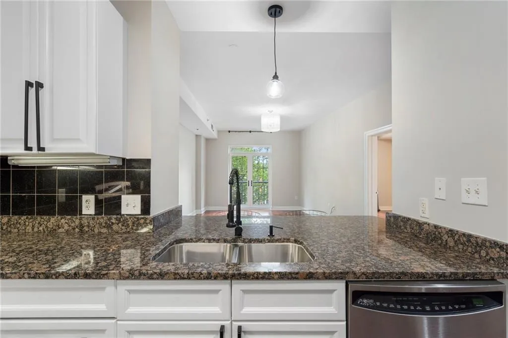 Kitchen featuring stainless steel dishwasher, a sink, white cabinets, backsplash, and dark stone counters