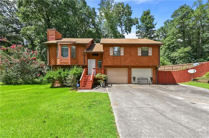 Wood-sided split-level residence featuring a two-car garage, red privacy fence, and concrete driveway