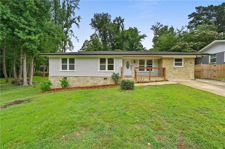Ranch-style exterior featuring stone and stucco finishes, a front porch with natural wood railing, a gravel driveway, and a front lawn with mature trees