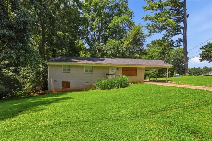 Brick exterior residence with a single-story design, front porch entry, attached carport, and a sloped, grassy lawn