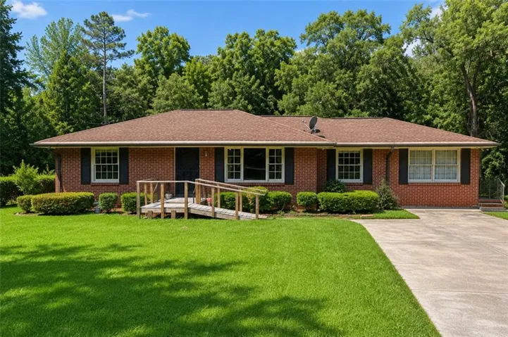 Brick exterior with a brown shingle roof, featuring white-framed windows, dark shutters, and a concrete driveway