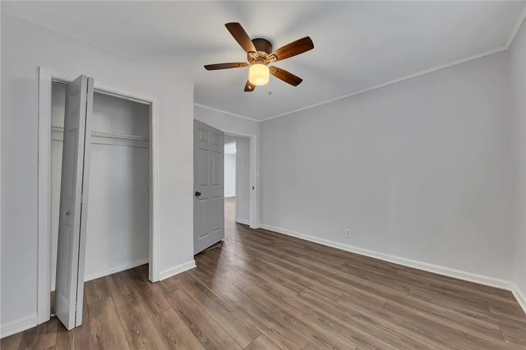 Unfurnished bedroom with wood finished floors, a closet, baseboards, ornamental molding, and a ceiling fan