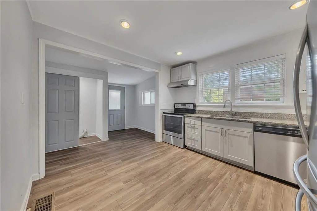 Kitchen featuring stainless steel appliances, a sink, light wood finished floors, under cabinet range hood, and baseboards