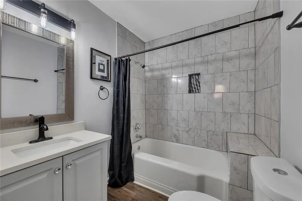 Bathroom featuring toilet, shower / bath combination with curtain, vanity, and wood finished floors