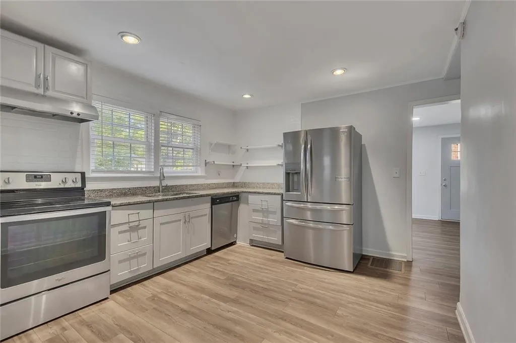 Kitchen with appliances with stainless steel finishes, a sink, under cabinet range hood, baseboards, and light wood finished floors