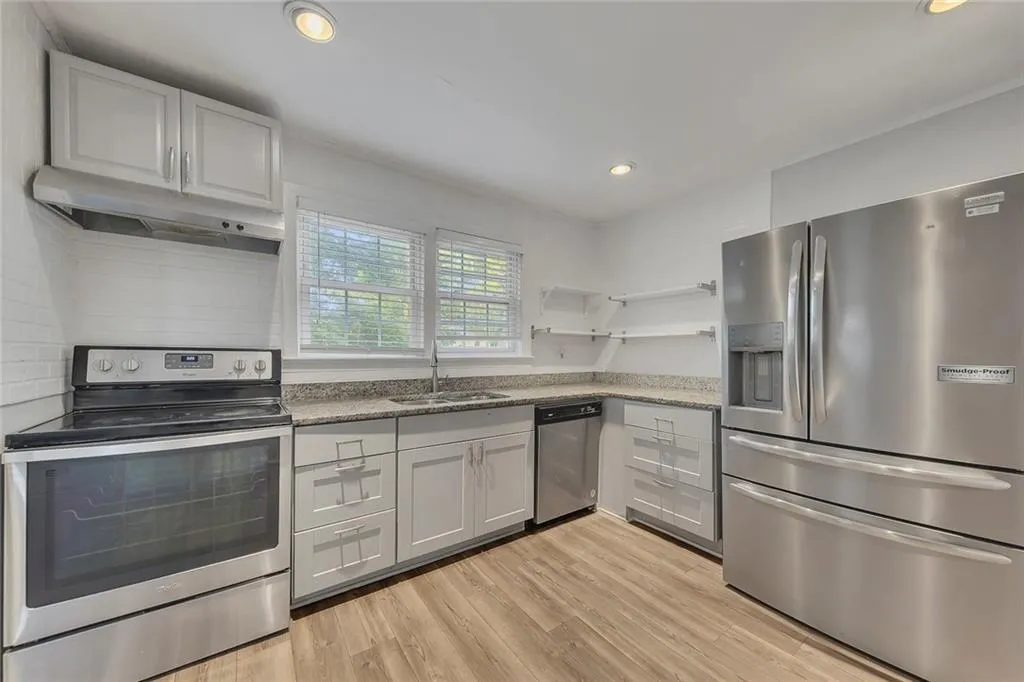 Kitchen featuring appliances with stainless steel finishes, a sink, open shelves, under cabinet range hood, and light wood-style flooring