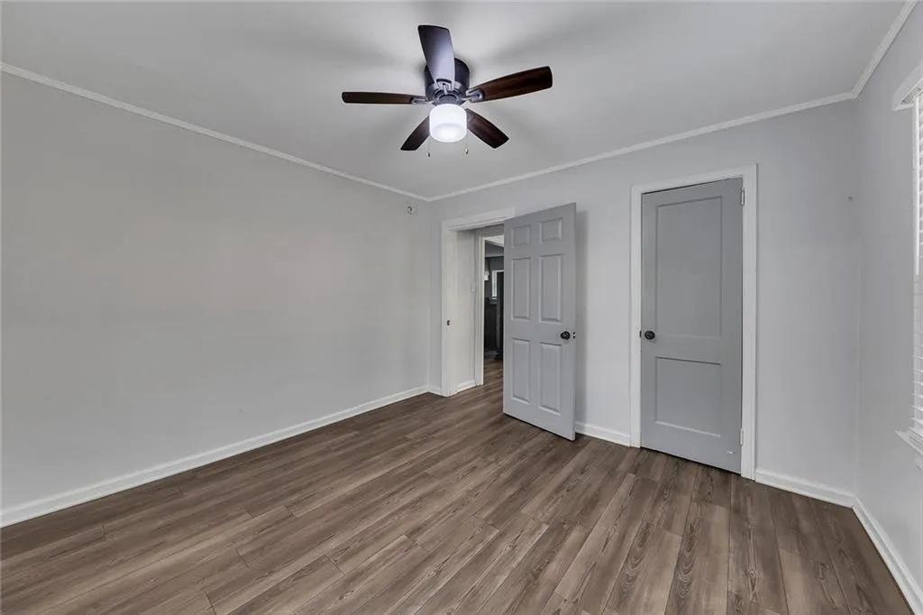 Unfurnished bedroom with dark wood finished floors, baseboards, crown molding, and a ceiling fan