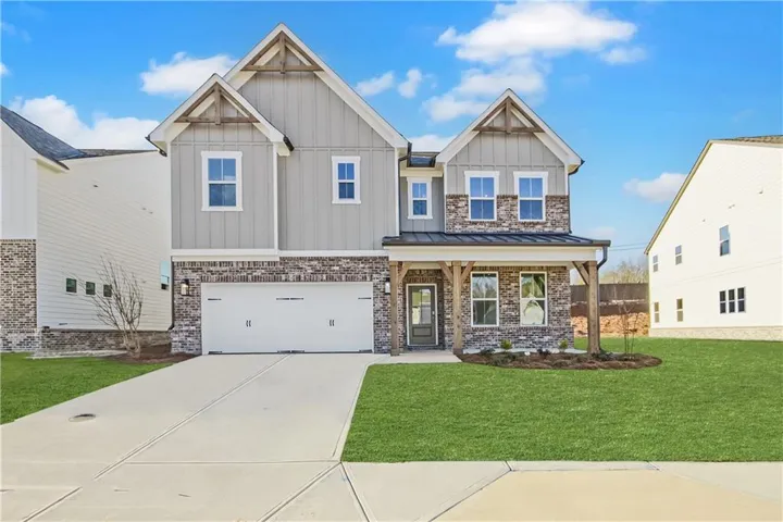 Two-story residence featuring a stone and siding exterior, an attached two-car garage, a covered front porch with timber-style columns, and a concrete driveway