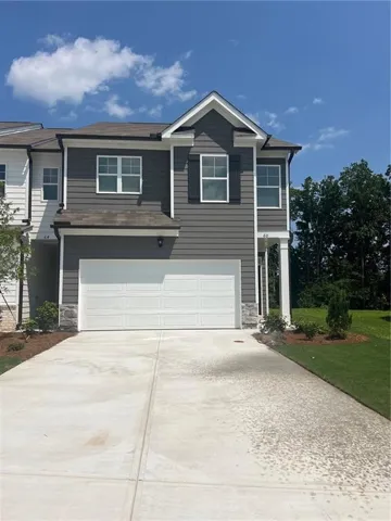 Two-story home featuring a clean driveway with concrete finish, white garage doors with panel detailing, and neutral gray exterior siding