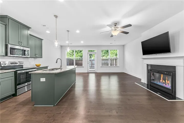 Open-concept living space featuring wood-finish flooring, a kitchen island with pendant lighting, stainless steel appliances, a fireplace with a mantel, and multiple windows