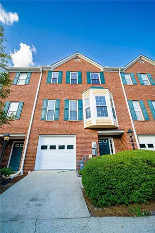 Brick townhome featuring a two-car garage with white paneled doors, multi-pane blue-trimmed windows, and a gabled roofline with peaked dormers