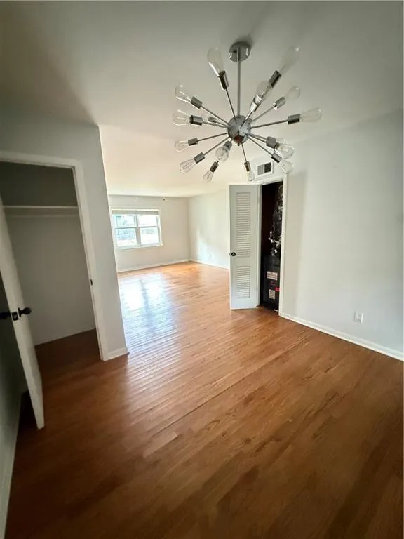 Open-concept living space featuring wood-finish flooring, a modern sputnik chandelier, white painted walls, and a window providing natural light