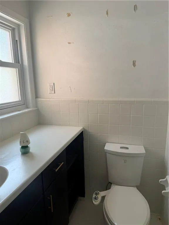 White tiled walls with a vanity featuring dark cabinetry and a light-toned countertop